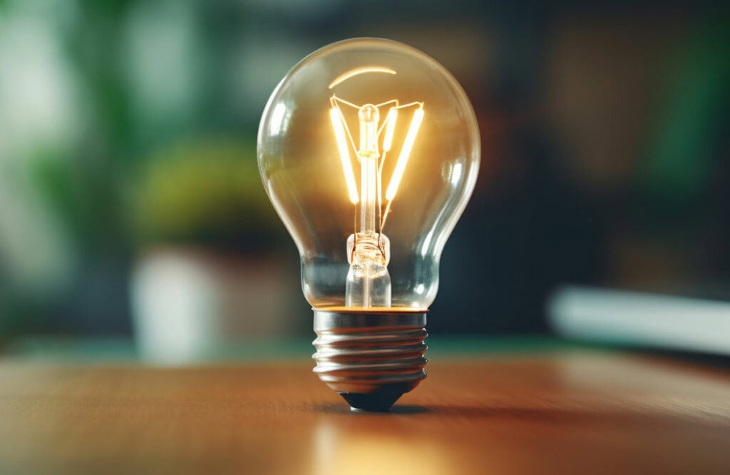 Glowing light bulb on the table in home office, working with creativity and save energy concept background. Generative AI
